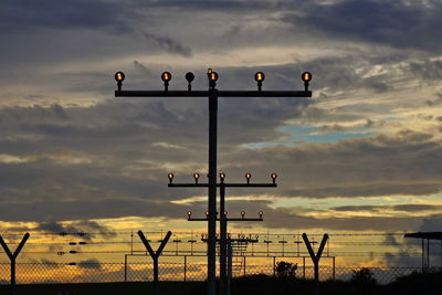 Low angle view of airport lights against sky during sunset