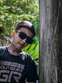 Portrait of boy wearing sunglasses standing by tree trunk