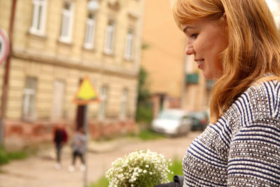 Woman smiling on street and holding white flowers. 40s smiling woman. copy space. outside portrait