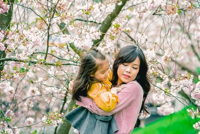 Beautiful young woman carrying daughter by cherry tree