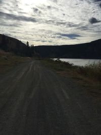 Empty road along countryside lake against cloudy sky