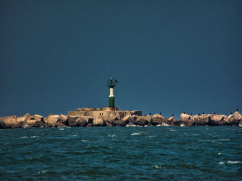 Lighthouse by sea against clear sky