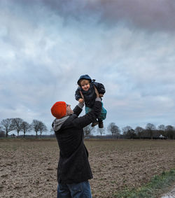 Father carrying daughter while standing on field against sky