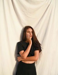Portrait of smiling young woman standing against wall