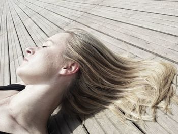 Close-up of young woman lying on boardwalk during sunny day