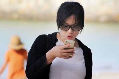 Young woman using mobile phone while standing at beach