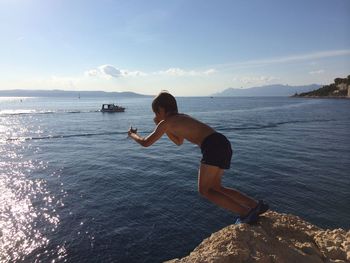 Full length of shirtless boy diving from rock into sea