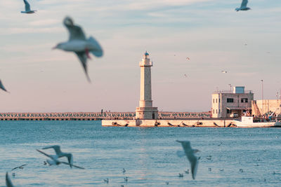 Beautiful lighthouse with calm blue sea, seagulls and fishing boat parked near the quay of the port