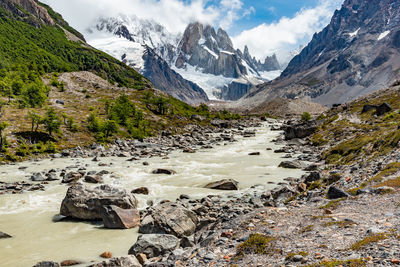 Scenic view of stream amidst snowcapped mountains against sky