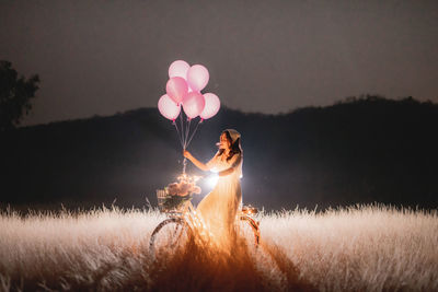 Side view of man holding balloons at field against sky at night