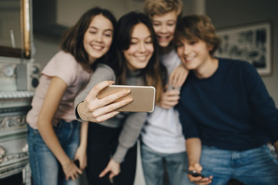 Happy friends taking selfie through smart phone while standing at home