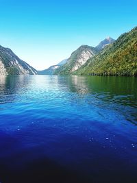 Scenic view of lake and mountains against clear blue sky