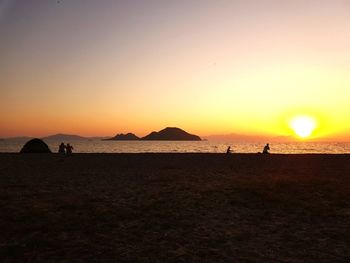 Silhouette people on beach against clear sky during sunset