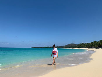 Rear view of woman standing at beach against clear blue sky