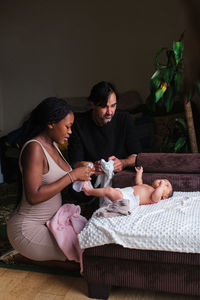 Caring african american mom changing diapers on infant lying on blanket with hispanic dad