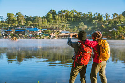 Rear view of people standing by lake against sky