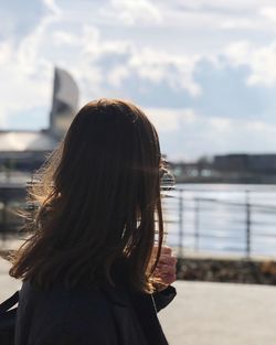 Rear view of woman standing by river against sky