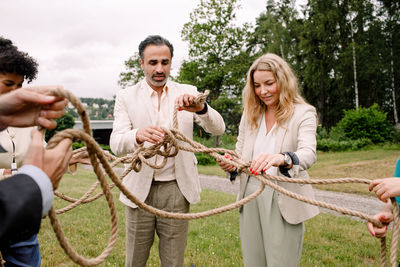 Male and female business professionals holding tangled rope while standing in lawn