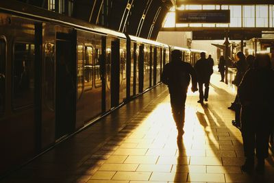 Commuters waiting by train at railroad station platform on sunny day