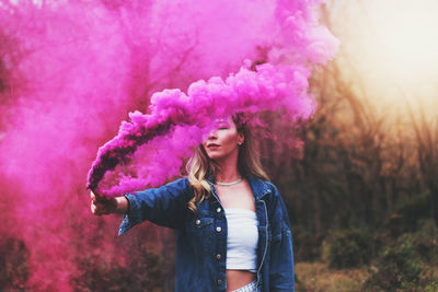 Young woman holding distress flare while standing at forest