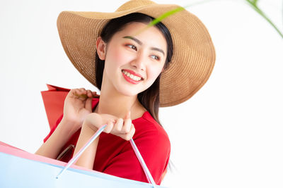 Portrait of happy young woman holding hat against white background