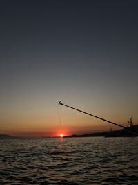 Silhouette fishing rod over sea against sky during sunset