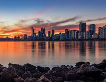 Sea by buildings against sky during sunset