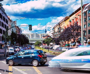 Cars on city street by buildings against sky