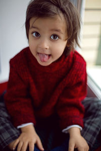 Boy child in red knitted sweater and hat sitting on the window in autumn