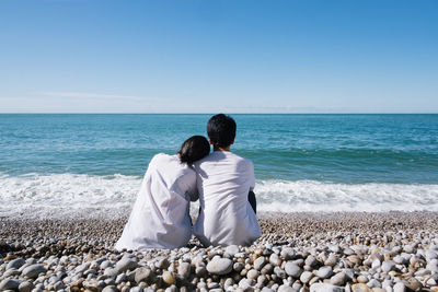 Rear view of couple sitting at beach against sky