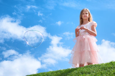 Low angle view of girl standing by bubble in mid-air against sky