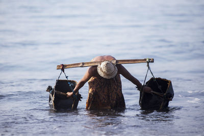 Shirtless man filling water in containers from lake