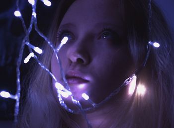 Close-up of young woman with illuminated string lights