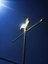 Low angle view of illuminated bird perching against clear blue sky