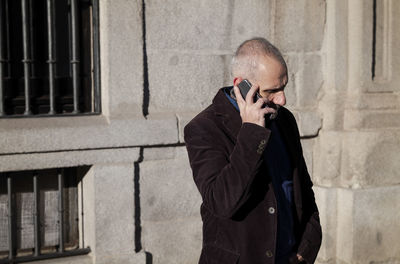 Adult man in suit talking on mobile phone against white stone wall