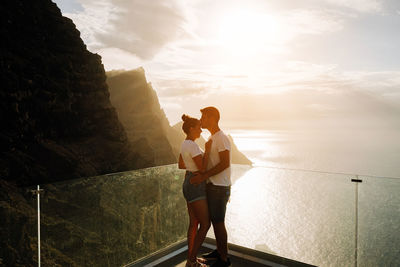 Side view of woman standing against sea against sky during sunset