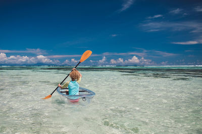 Rear view of woman rowing on sea against sky