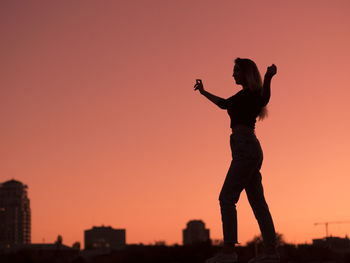 Side view of woman standing against clear sky during sunset