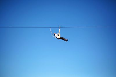 Low angle view of woman performing stunt on rope against clear blue sky
