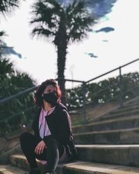 Young woman wearing sunglasses standing by railing against trees