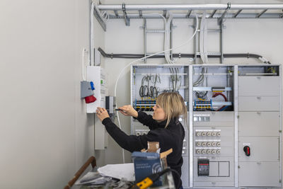 Female technician installing fuse box in control room at industry