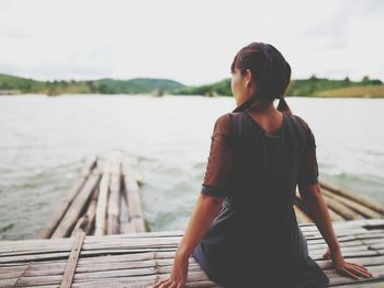 Woman standing on pier over lake against sky