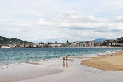 Rear view of men walking at beach against cloudy sky