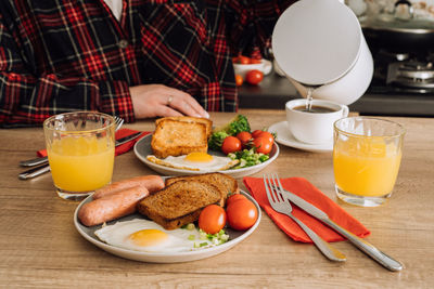 Woman pours water into a cup, prepares to enjoy an english breakfast with coffee and orange juice