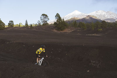 Female cyclist riding bike on dirt road with snowy mount teide in back