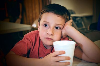 Close-up of thoughtful boy holding glass at home