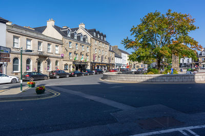 Road by buildings in city against clear blue sky