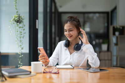 Young woman using mobile phone while sitting on table