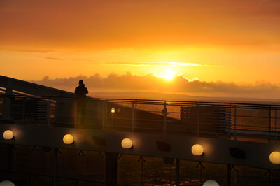 Silhouette railing by sea against orange sky