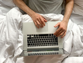 Middle aged adult man using laptop at home in bed vibes white bedsheets early morning working